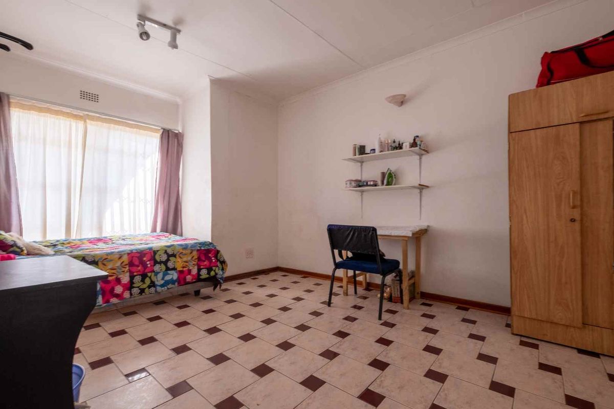 A functional bedroom featuring tiled flooring, a built-in wardrobe, and a large window allowing for natural light.