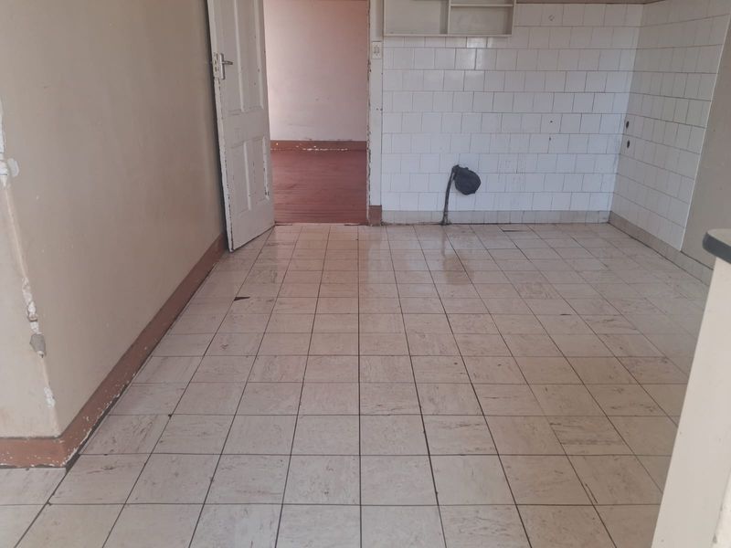 An empty, dated kitchen area featuring tiled flooring and splashbacks, requiring renovation to modernize the space.
