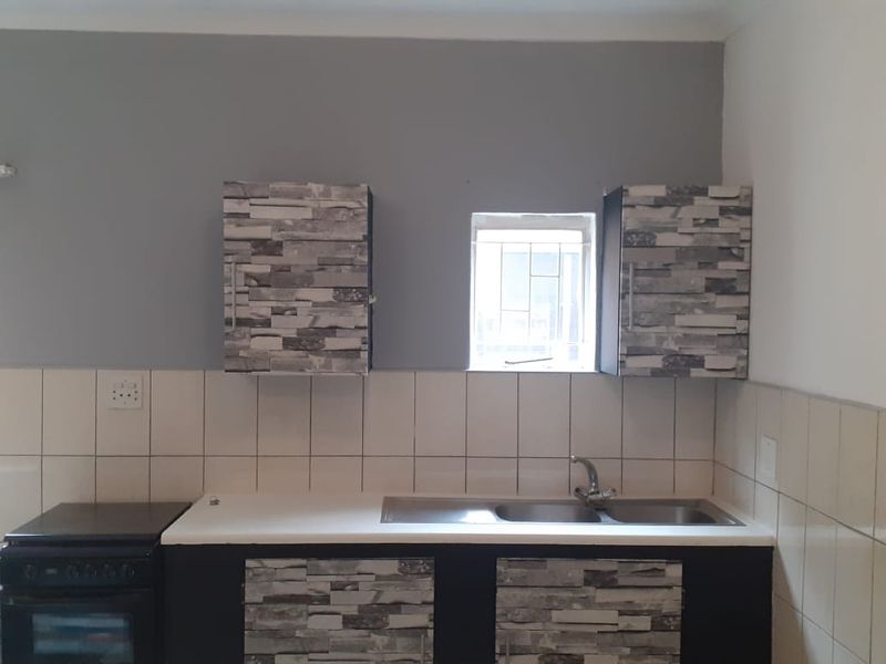 A functional kitchen area featuring built-in cabinetry, a stainless steel double sink, and a freestanding stove with tiled splashbacks.