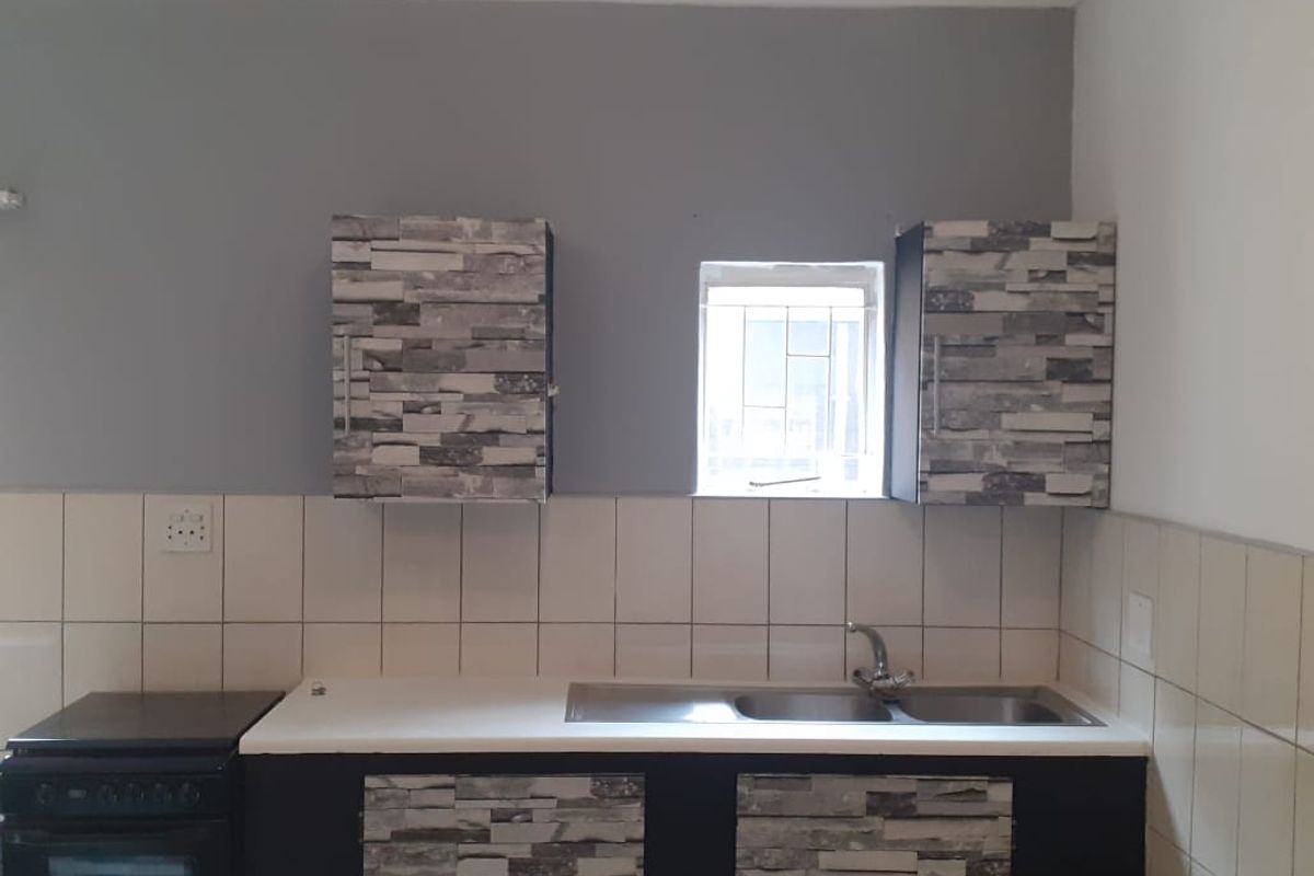 A functional kitchen area featuring built-in cabinetry, a stainless steel double sink, and a freestanding stove with tiled splashbacks.