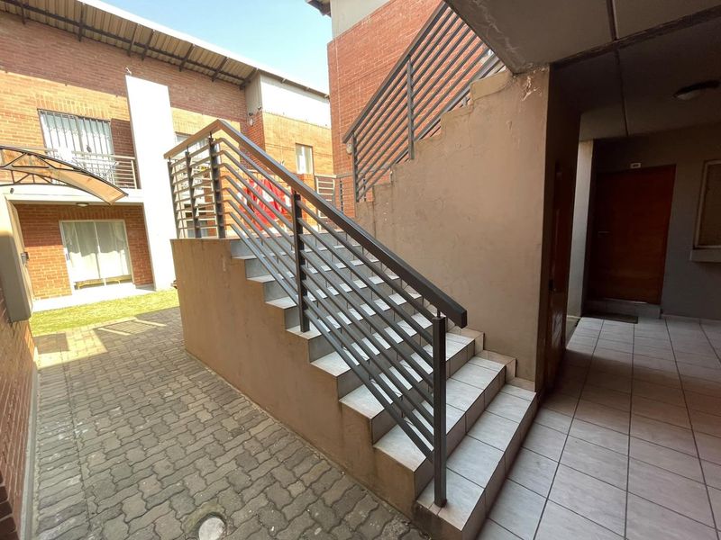 Exterior view of a residential apartment complex featuring a paved courtyard, brick facade, and a tiled staircase with metal railings.
