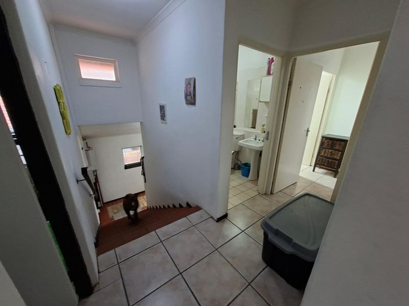 A tiled hallway area featuring a staircase with a handrail, providing access to adjacent rooms and a bathroom.