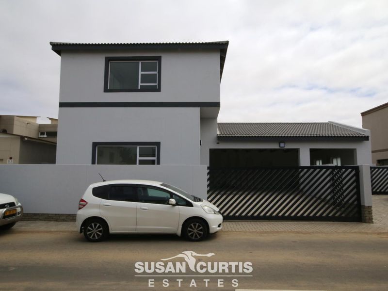 Modern two-story residential property featuring a clean grey facade, tiled roof, and a secure gated driveway with integrated garage space.