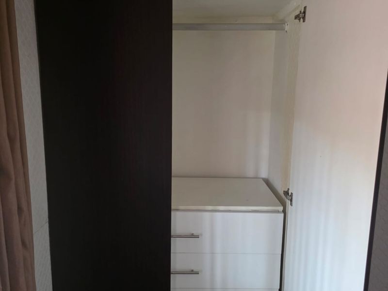 A bedroom featuring a built-in wardrobe with dark exterior doors, internal white shelving, integrated drawers, and a hanging rail.