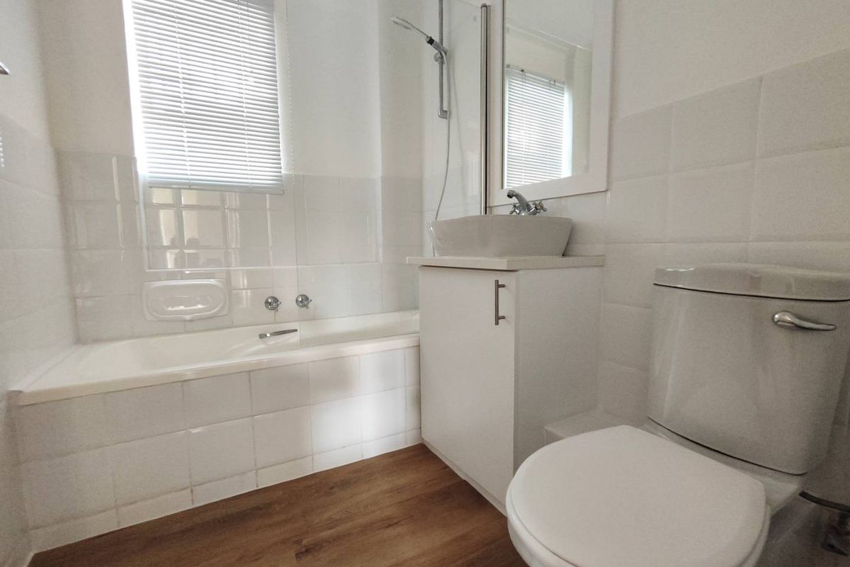 A compact bathroom featuring a white bathtub with shower mixer, a vanity unit with a vessel sink, and a standard toilet.