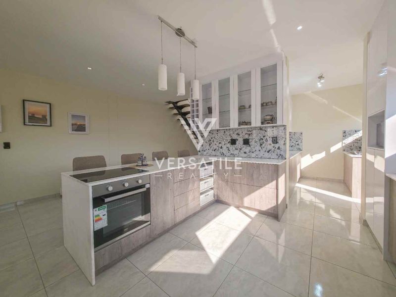 Modern kitchen featuring a central island with built-in oven, terrazzo-style backsplash, glass-fronted cabinetry, and sleek tiled flooring.