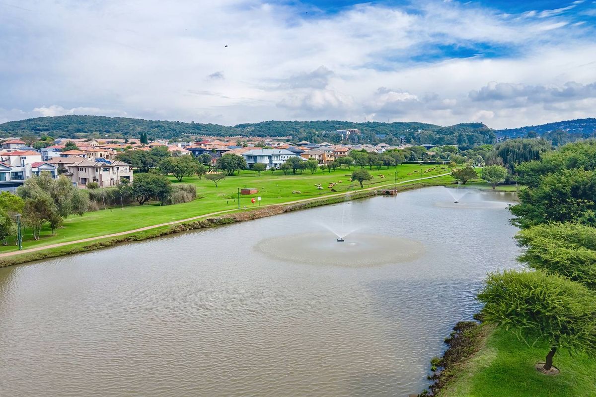 Aerial view of a scenic estate lake with water fountains, surrounded by landscaped green spaces and residential properties.