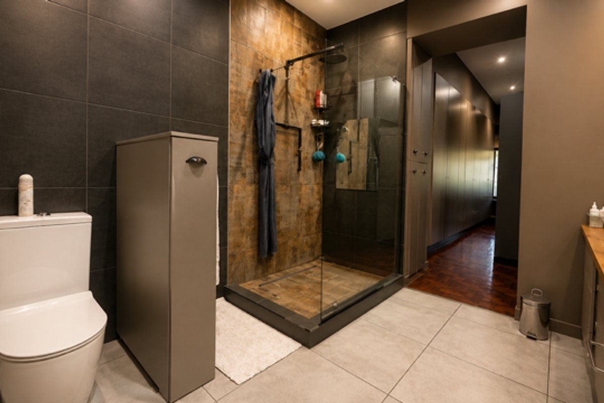 Modern bathroom featuring a walk-in shower with glass enclosure, dark tiled walls, dual vanity with wooden countertop, and sleek contemporary fixtures.