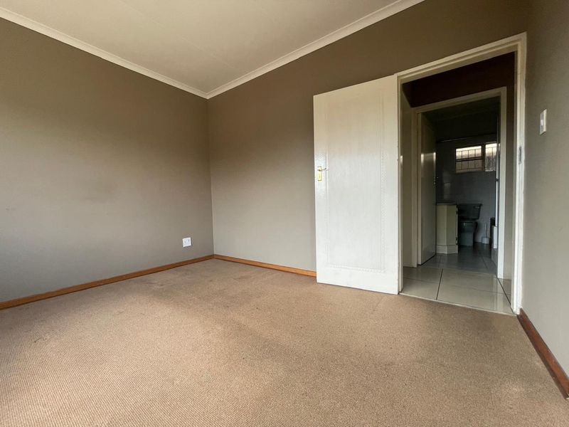An empty bedroom featuring carpeted flooring and neutral wall paint, with an adjacent doorway leading to a bathroom area.