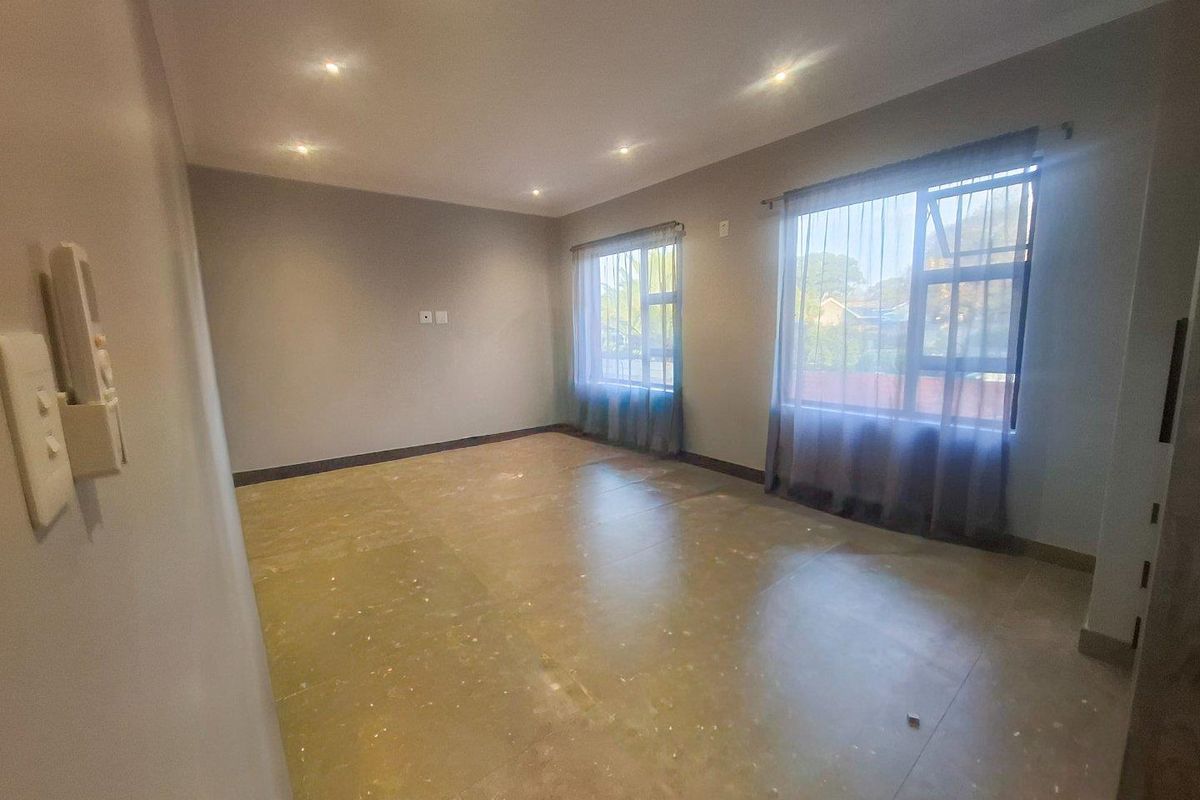 A spacious, empty bedroom featuring neutral walls, recessed ceiling lighting, and large windows with natural light.