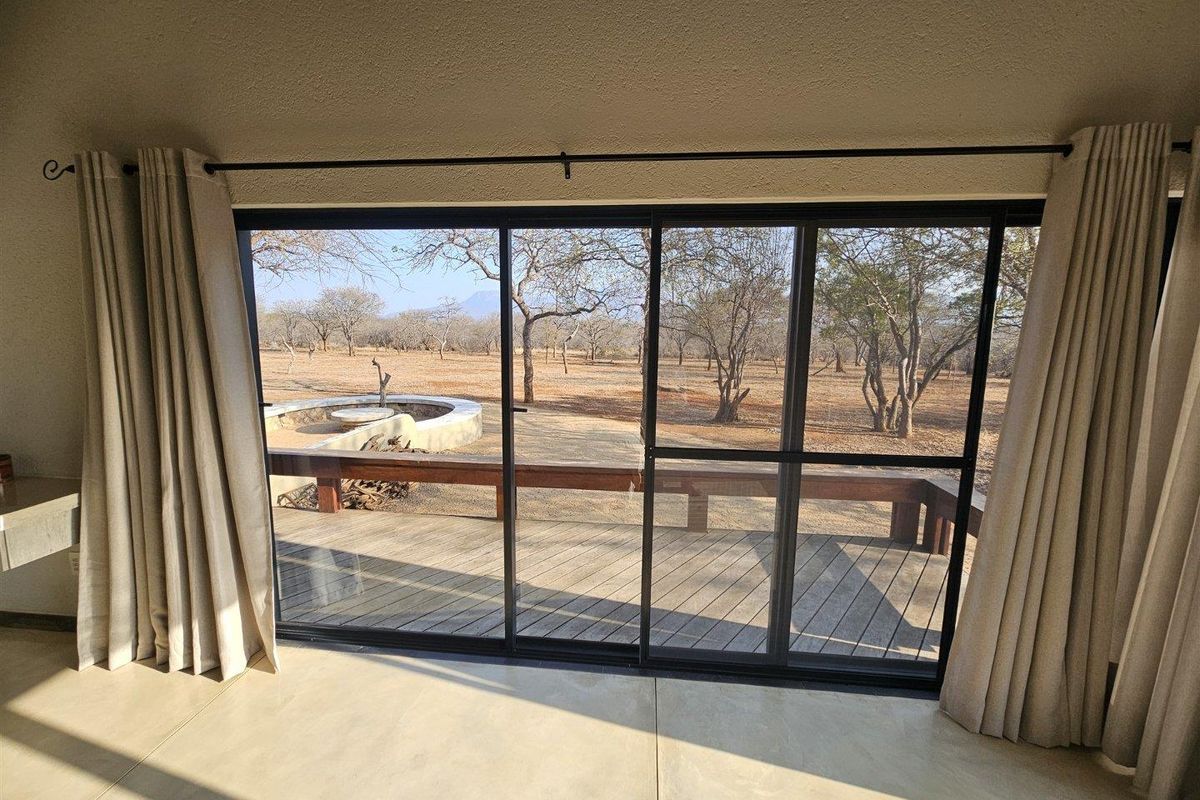 Bright living area featuring large sliding glass doors that open onto a wooden deck with a built-in fire pit and scenic bushveld views.
