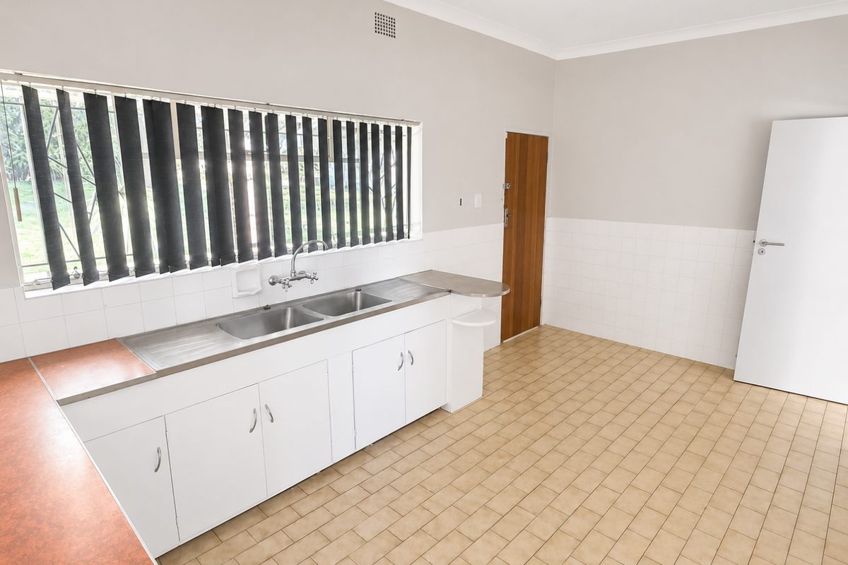 A functional kitchen area featuring white cabinetry, a double stainless steel sink, tiled splashbacks, and neutral floor tiles.