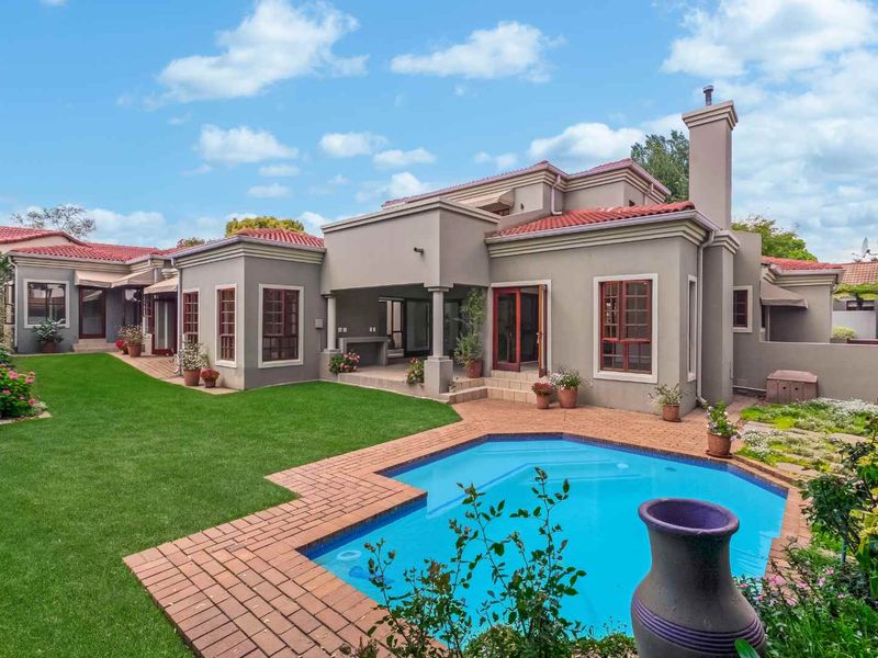 Rear view of the property featuring a well-maintained garden, swimming pool with brick surround, and a covered patio area.