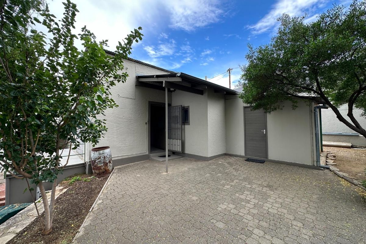 A paved rear courtyard area featuring a covered entrance, solid exterior doors, and established trees, providing a functional outdoor space.