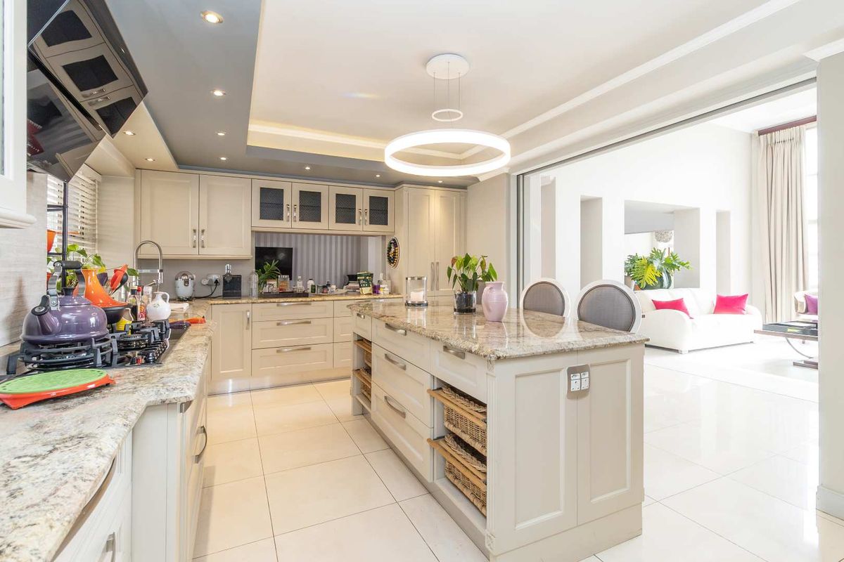 Modern kitchen featuring a central island with granite countertops, built-in cabinetry, integrated hob, and recessed ceiling lighting, flowing into an open-plan living area.