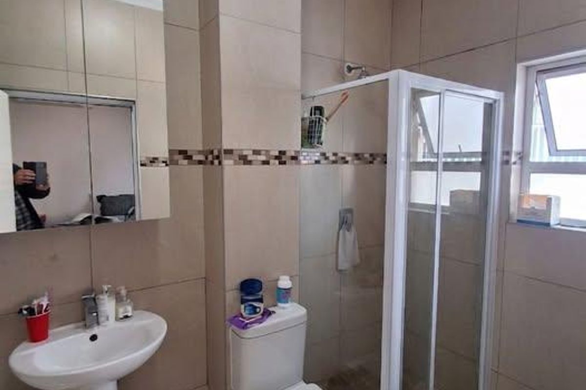 A functional bathroom featuring a pedestal basin, toilet, and a glass-enclosed shower with tiled finishes throughout.