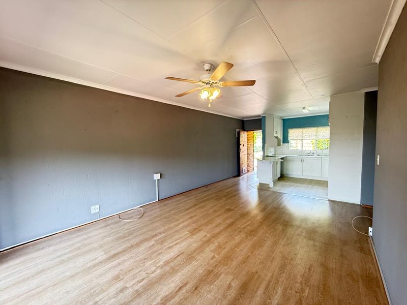 An open-plan living area featuring laminate flooring, a ceiling fan, and an adjoining kitchen space with built-in cabinetry.