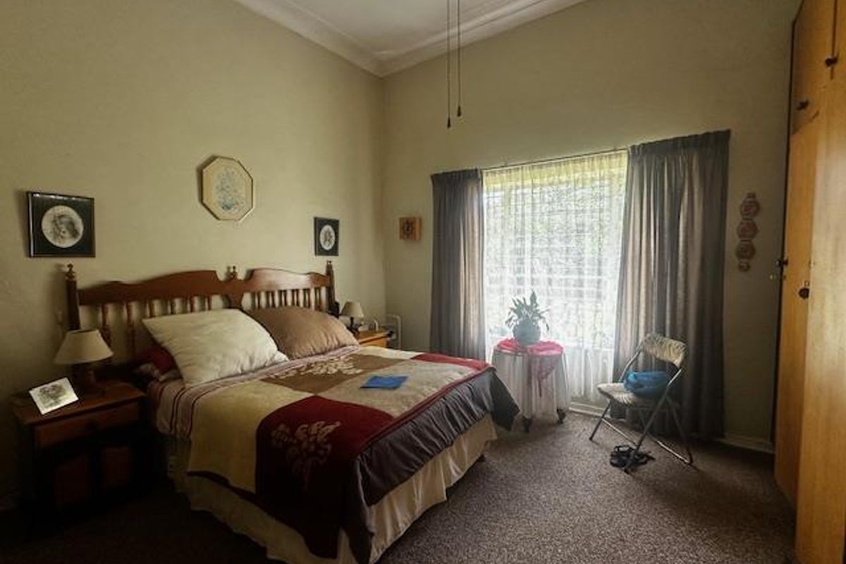 A spacious bedroom featuring high ceilings, built-in wooden cabinetry, and large windows with curtains, offering a comfortable and traditional living space.