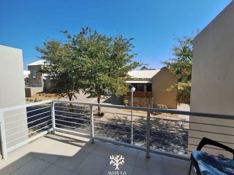 A clean, open-air balcony featuring tiled flooring and a modern metal balustrade, offering a clear view of the surrounding residential complex.