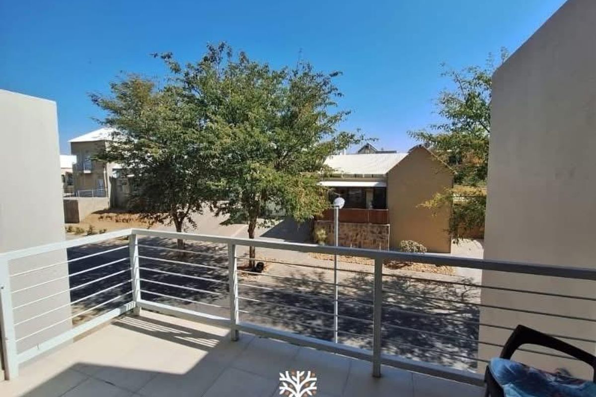 A clean, open-air balcony featuring tiled flooring and a modern metal balustrade, offering a clear view of the surrounding residential complex.