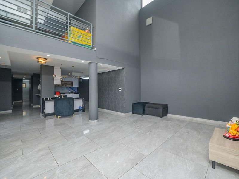 Spacious open-plan living area featuring high ceilings, a mezzanine level with metal railing, modern porcelain tile flooring, and a contemporary feature wall.