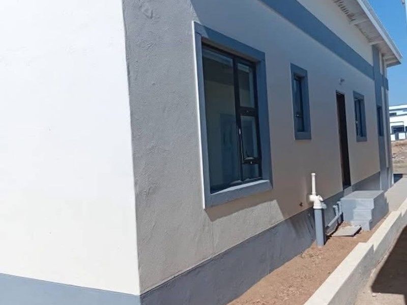 A view of the rear exterior facade of the townhouse, featuring clean plastered walls, aluminium window frames, and an unfinished garden area.