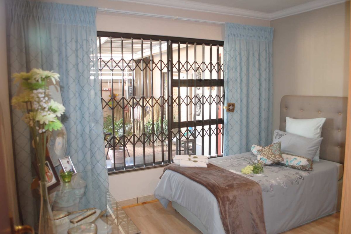 A bedroom featuring laminate flooring and a sliding door with a security gate leading to an outdoor patio area.
