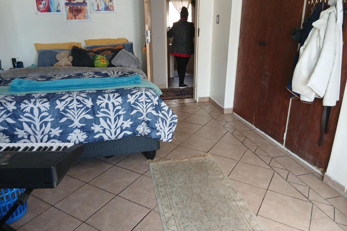 A bedroom featuring tiled flooring and built-in wooden cupboards, with direct access to an adjoining room.