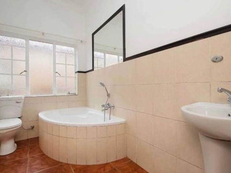 A functional bathroom featuring a corner bathtub, pedestal sink, toilet, and neutral wall tiling with a tiled floor.