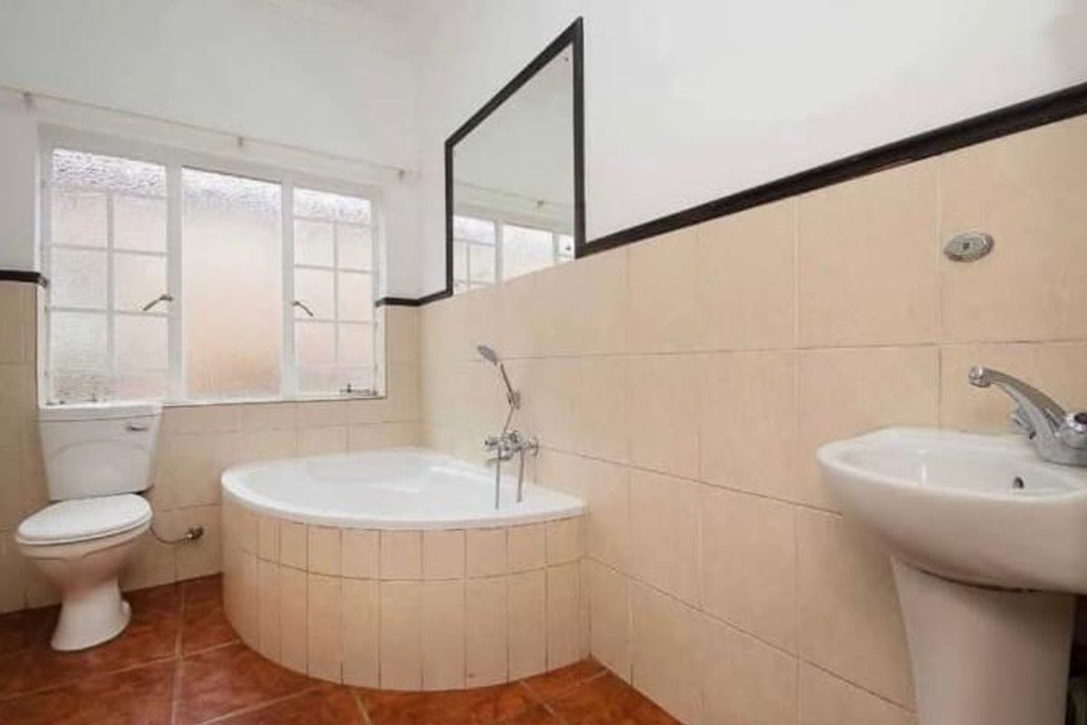 A functional bathroom featuring a corner bathtub, pedestal sink, toilet, and neutral wall tiling with a tiled floor.