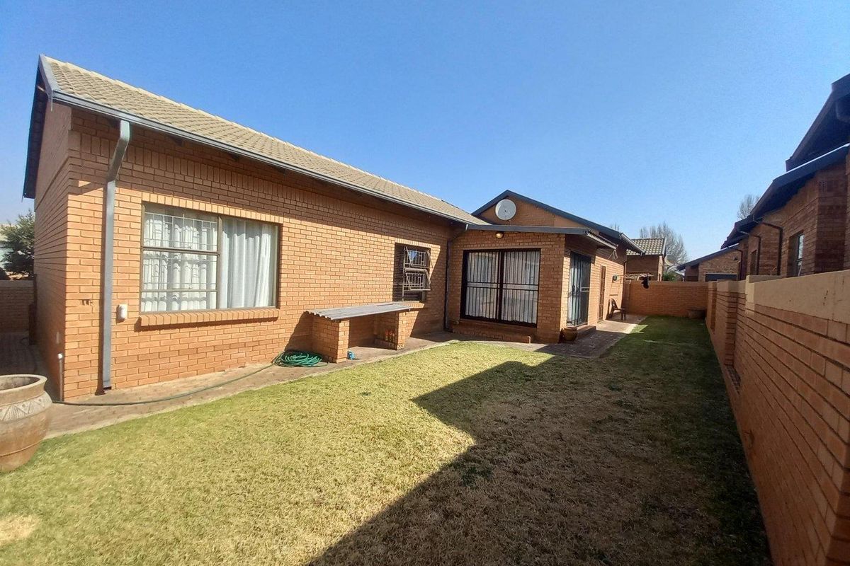 Rear view of the townhouse featuring a private garden, brick exterior walls, security-fitted windows, and a built-in brick braai area.