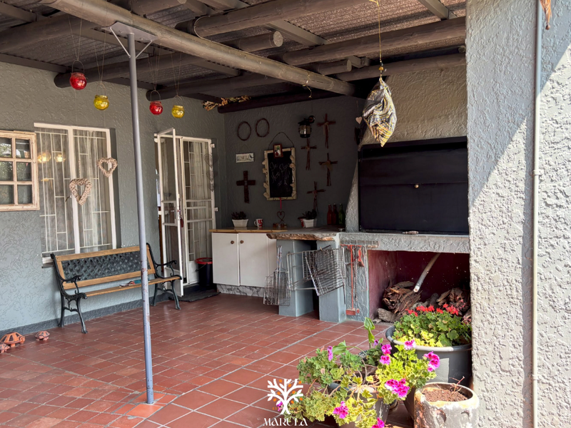 Covered patio area featuring a built-in braai, tiled flooring, and exposed beam ceiling, providing a functional outdoor entertainment space.