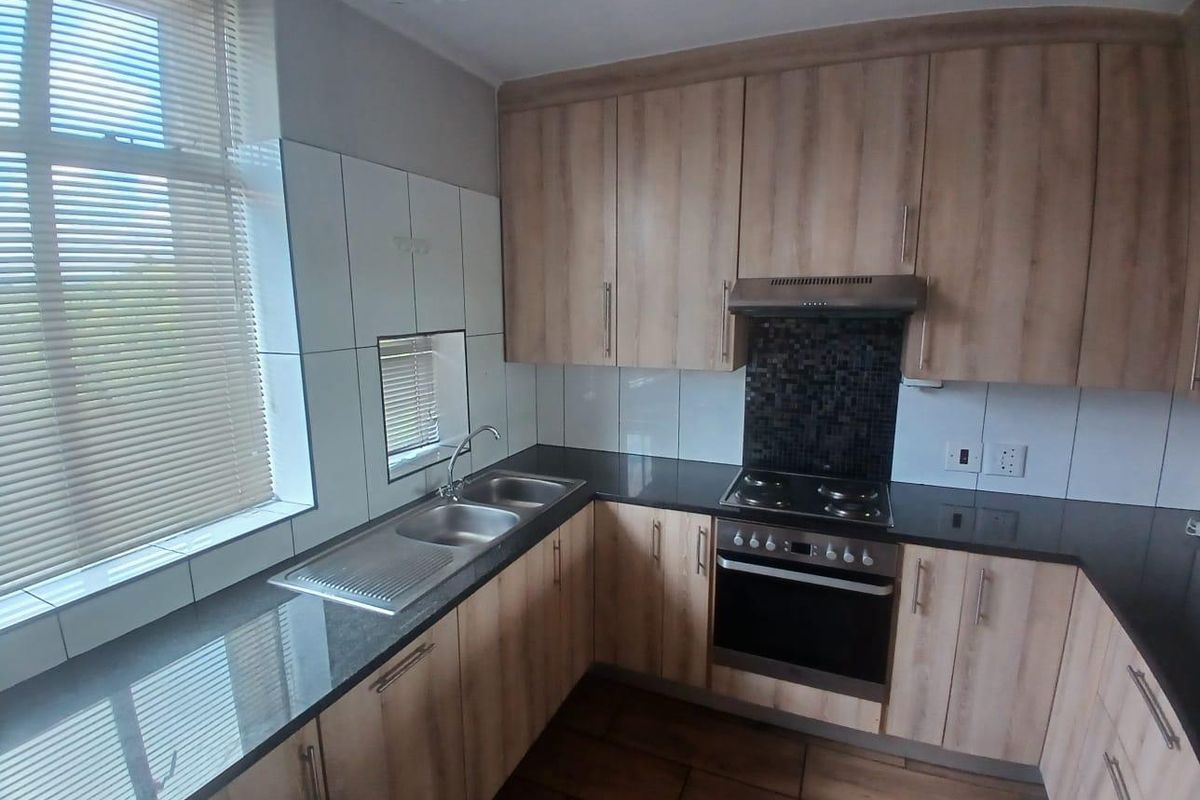 A modern, well-maintained kitchen featuring light wood-finish cabinetry, dark granite countertops, a built-in oven, and a double stainless steel sink.