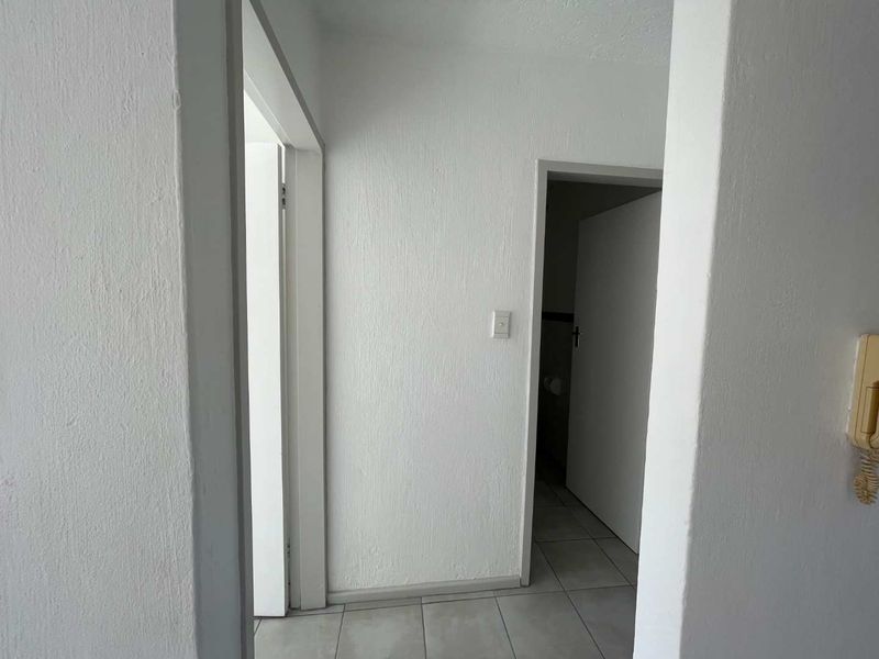 A simple, neutral hallway featuring tiled flooring and an intercom system, providing access to adjacent rooms.