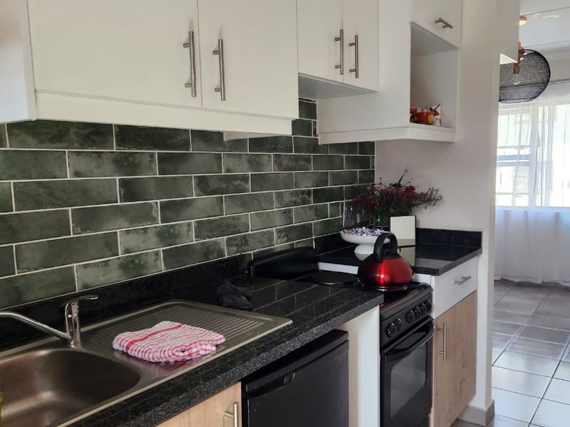 A functional kitchen featuring modern white and wood-grain cabinetry, dark granite countertops, a green subway tile backsplash, and tiled flooring.