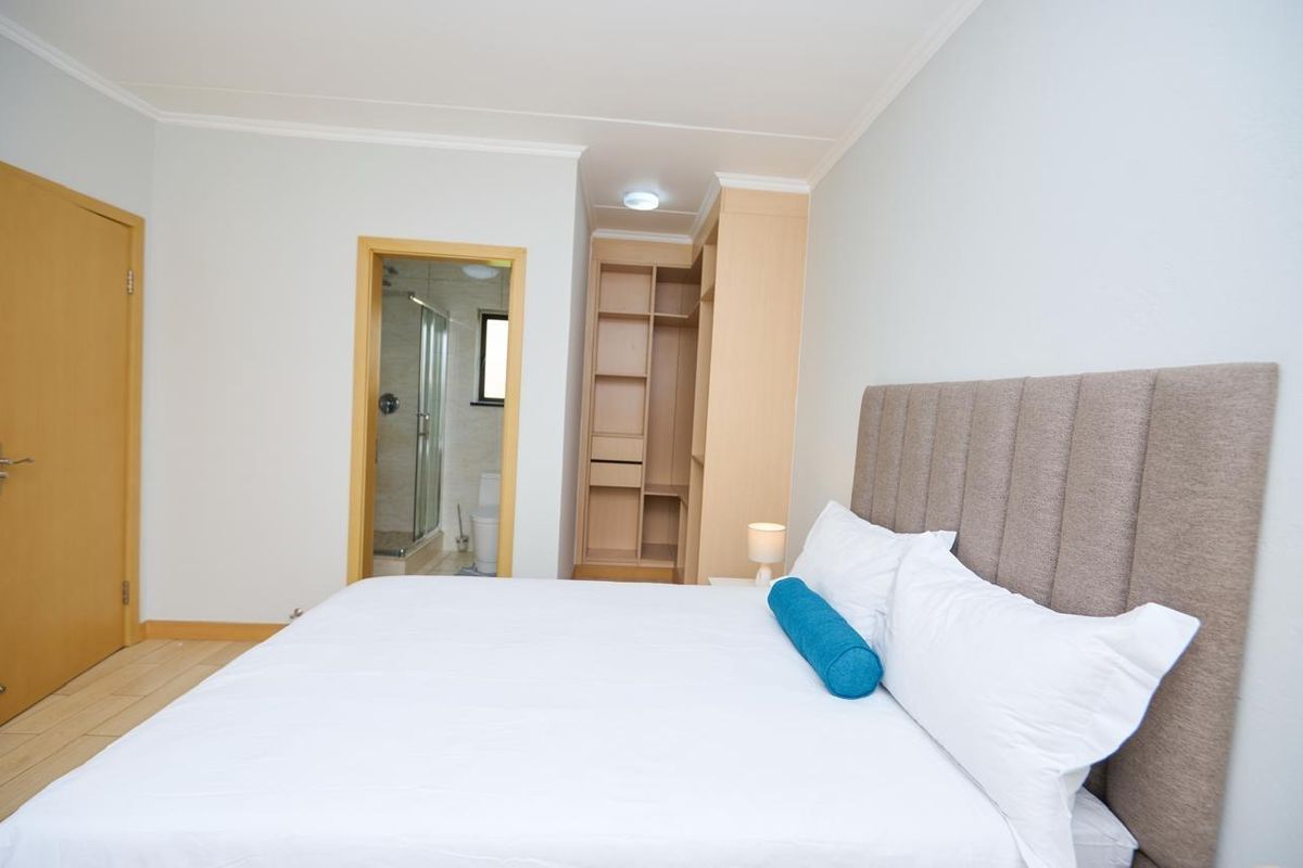 A well-maintained bedroom featuring built-in cabinetry and an adjoining en-suite bathroom with neutral finishes and tiled flooring.