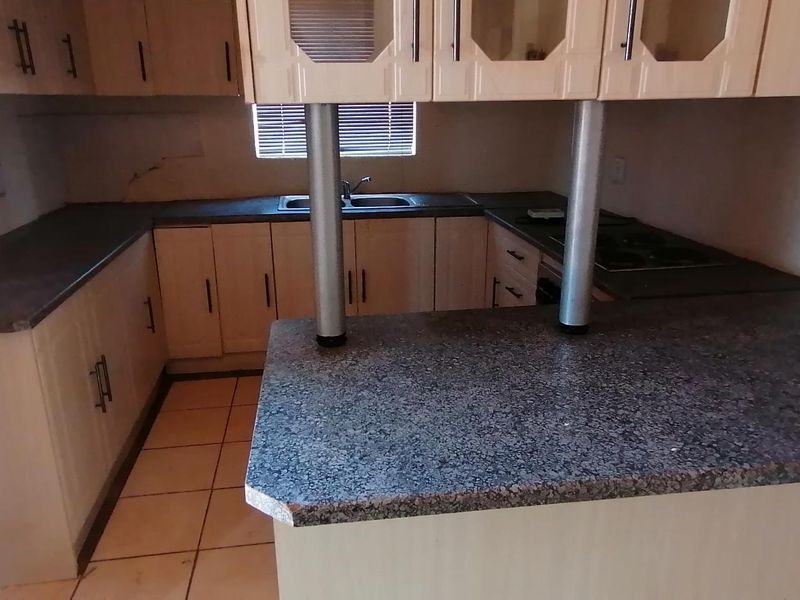 A functional kitchen featuring laminate cabinetry, granite countertops, a double basin sink, and a built-in hob with an integrated breakfast nook.