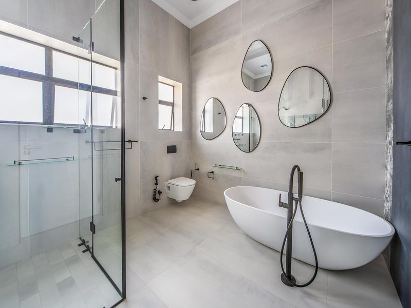 Modern bathroom featuring a freestanding bathtub, walk-in shower with glass enclosure, wall-mounted toilet, and contemporary grey tiling with matte black fixtures.