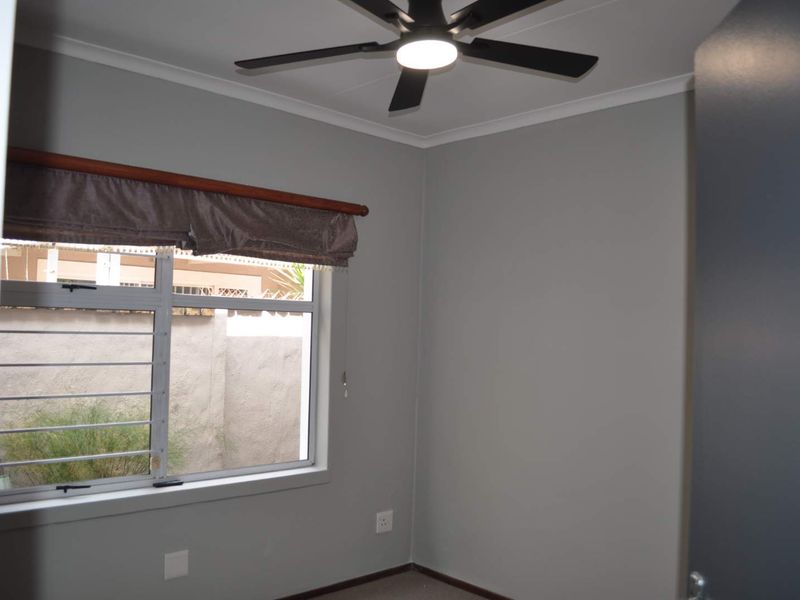 A clean, neutral-toned bedroom featuring a modern ceiling fan and an aluminium-framed window with security bars.