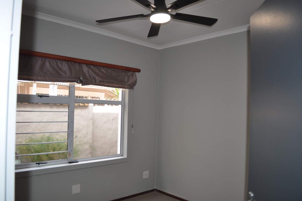 A clean, neutral-toned bedroom featuring a modern ceiling fan and an aluminium-framed window with security bars.
