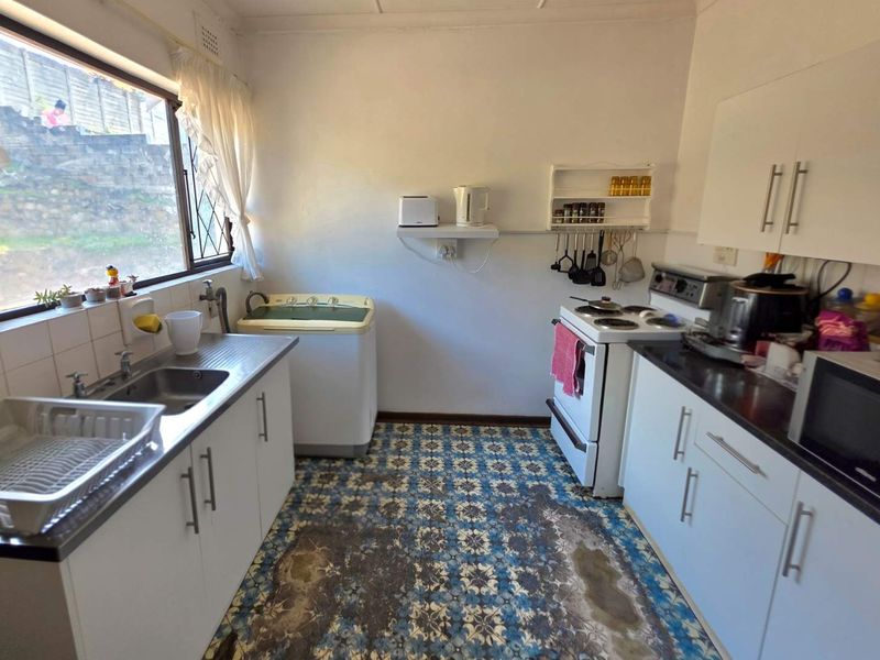 A functional kitchen featuring white cabinetry, a stainless steel sink, and a freestanding stove, with patterned floor tiles showing significant wear.
