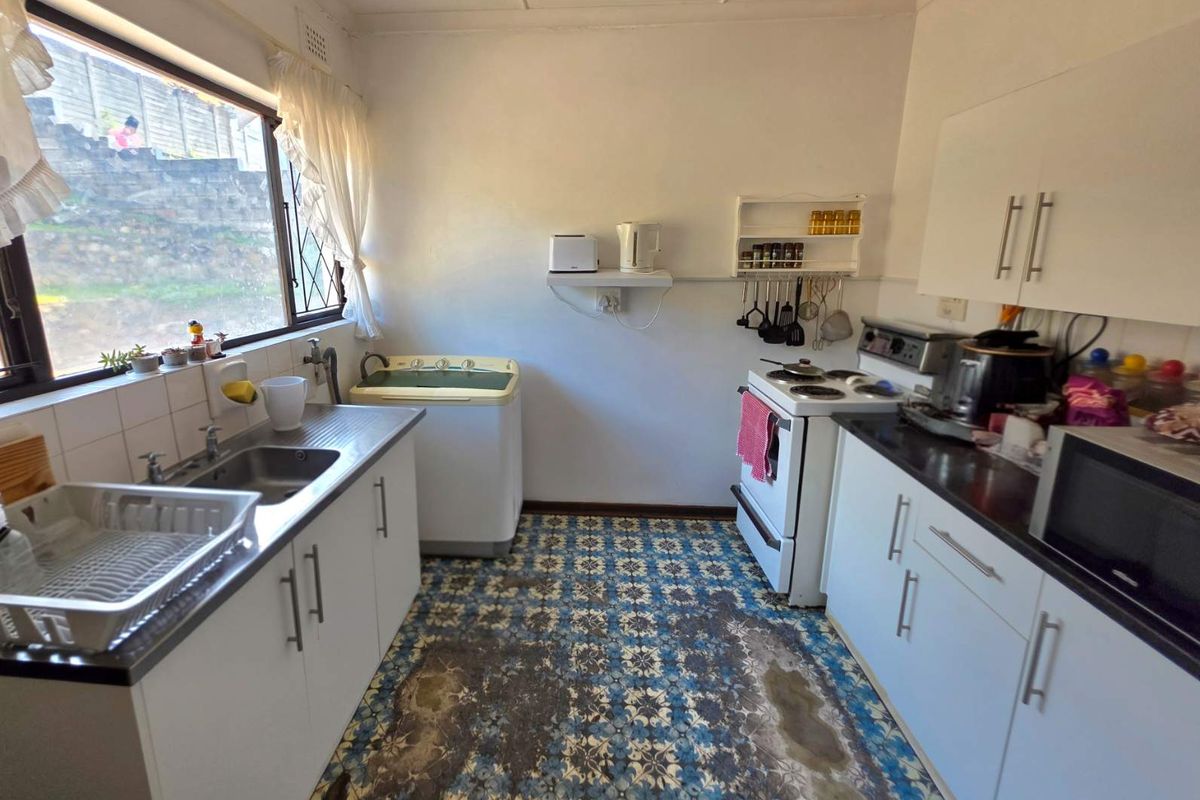 A functional kitchen featuring white cabinetry, a stainless steel sink, and a freestanding stove, with patterned floor tiles showing significant wear.