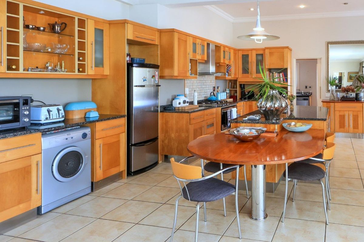 Spacious kitchen featuring warm-toned wooden cabinetry, granite countertops, a central island with integrated dining space, and tiled flooring throughout.
