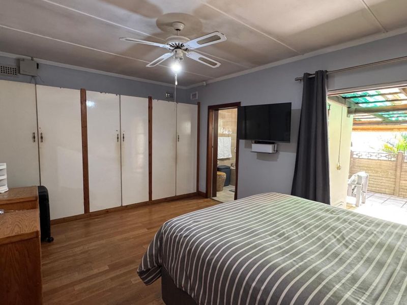 Spacious bedroom featuring built-in cupboards, laminate flooring, a ceiling fan, and direct access to an outdoor patio area.
