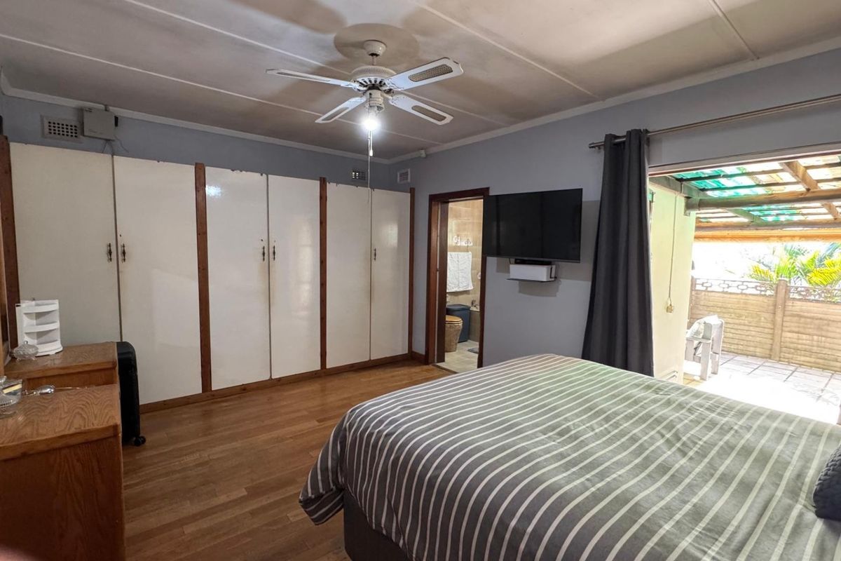 Spacious bedroom featuring built-in cupboards, laminate flooring, a ceiling fan, and direct access to an outdoor patio area.