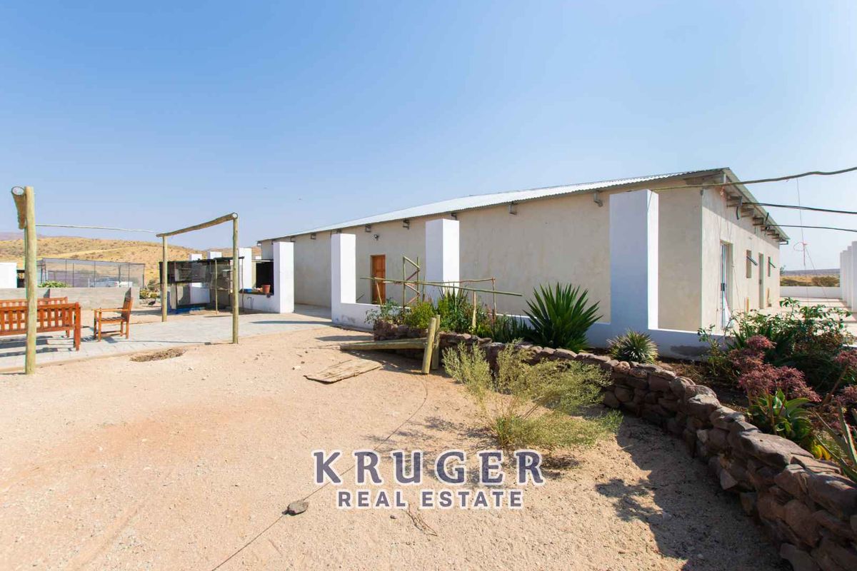 Rear view of the property featuring a covered patio area, stone retaining wall, and expansive outdoor space in a rural setting.