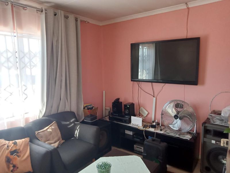 A living room featuring a wall-mounted television, security gate on the window, and coving. The space would benefit from cosmetic updates and cable management.