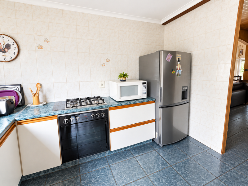 A functional kitchen featuring a gas hob, built-in oven, tiled splashback, and durable floor tiles, offering a practical layout for daily cooking.