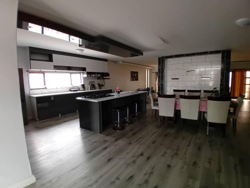 Spacious open-plan living area featuring a modern kitchen with a central island, gas hob, and sleek cabinetry, seamlessly flowing into the dining space.