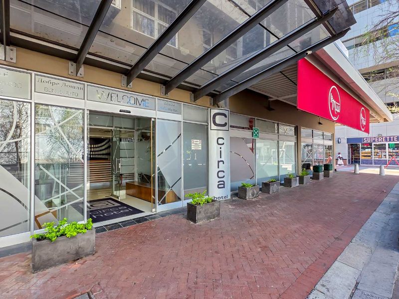 Front entrance of the Circa Hotel featuring a glass canopy, paved walkway, and modern glass facade with prominent signage.
